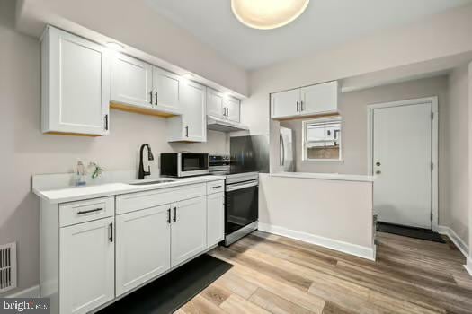 kitchen with white cabinetry, appliances with stainless steel finishes, sink, and light hardwood / wood-style floors