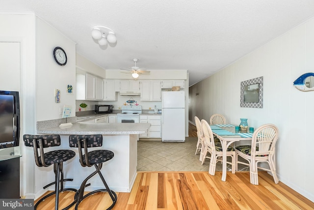 kitchen with a kitchen bar, white cabinetry, light hardwood / wood-style flooring, kitchen peninsula, and white appliances