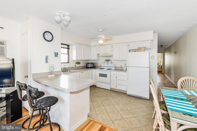 kitchen with sink, white appliances, a breakfast bar, white cabinetry, and kitchen peninsula