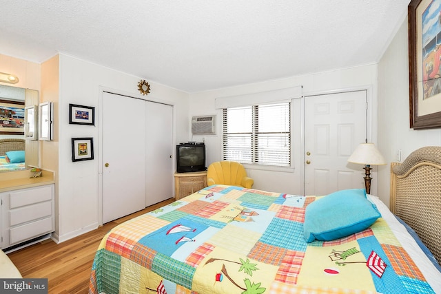 bedroom featuring a wall mounted air conditioner, a closet, a textured ceiling, and light wood-type flooring