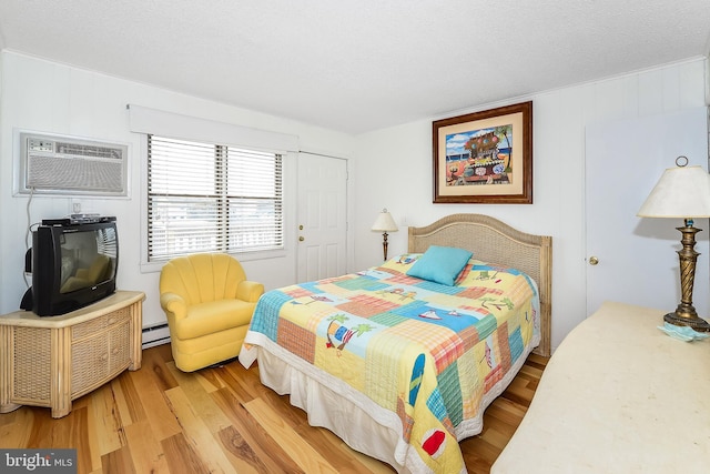 bedroom with a wall mounted air conditioner, wood-type flooring, a textured ceiling, and a baseboard heating unit