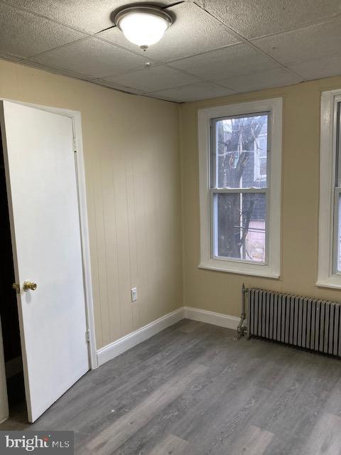 empty room with a paneled ceiling, radiator, and hardwood / wood-style floors