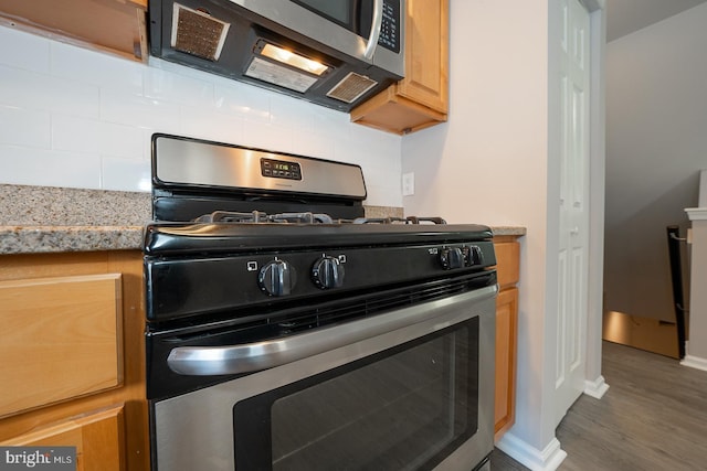 kitchen with light stone countertops, appliances with stainless steel finishes, dark wood-type flooring, and decorative backsplash