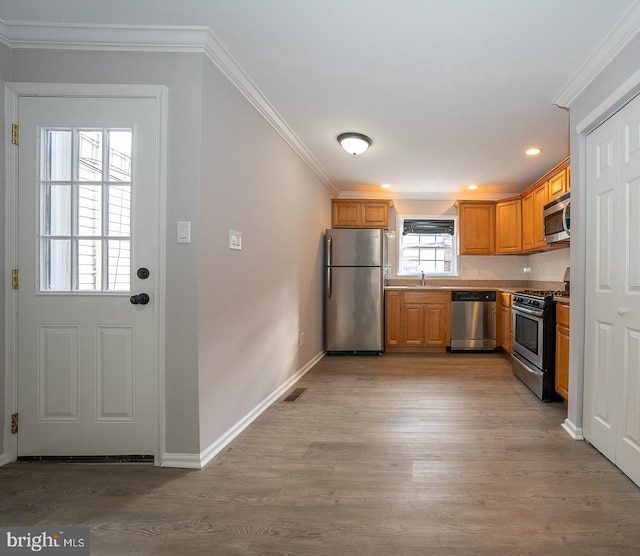 kitchen with ornamental molding, light hardwood / wood-style floors, and appliances with stainless steel finishes