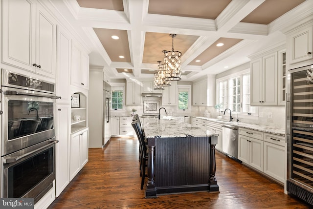 kitchen with a breakfast bar, a kitchen island with sink, stainless steel appliances, white cabinets, and decorative light fixtures