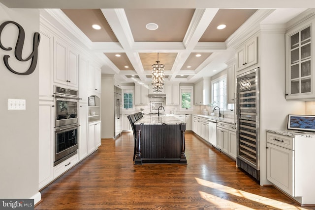 kitchen featuring white cabinetry, appliances with stainless steel finishes, light stone countertops, and an island with sink