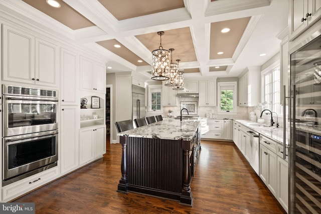 kitchen with sink, hanging light fixtures, stainless steel appliances, a kitchen island with sink, and white cabinets