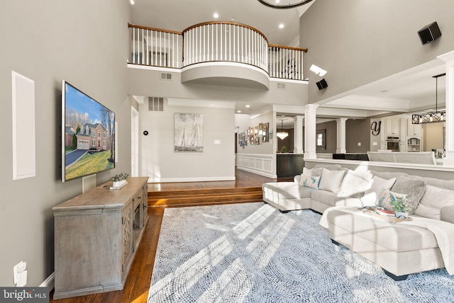 living room featuring a towering ceiling, decorative columns, and dark hardwood / wood-style floors