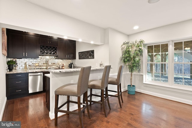 bar with sink, light stone counters, stainless steel dishwasher, dark hardwood / wood-style floors, and backsplash