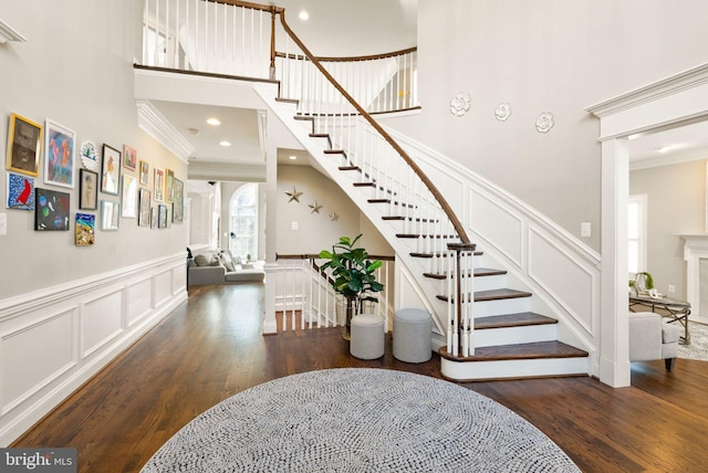 stairs with crown molding, wood-type flooring, and a towering ceiling