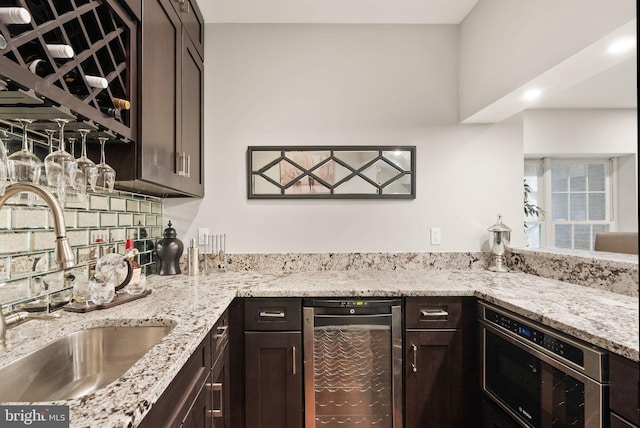 kitchen featuring wine cooler, dark brown cabinetry, sink, light stone counters, and backsplash