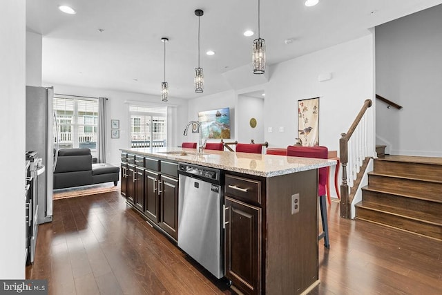 kitchen with appliances with stainless steel finishes, a kitchen bar, hanging light fixtures, dark brown cabinetry, and a center island with sink