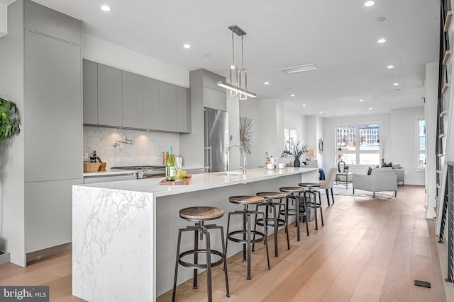 kitchen featuring a large island, gray cabinetry, stainless steel appliances, a kitchen breakfast bar, and decorative light fixtures