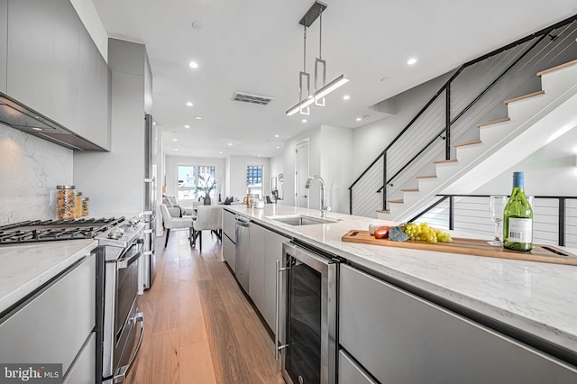 kitchen featuring gray cabinets, wine cooler, hanging light fixtures, stainless steel gas range, and light hardwood / wood-style flooring