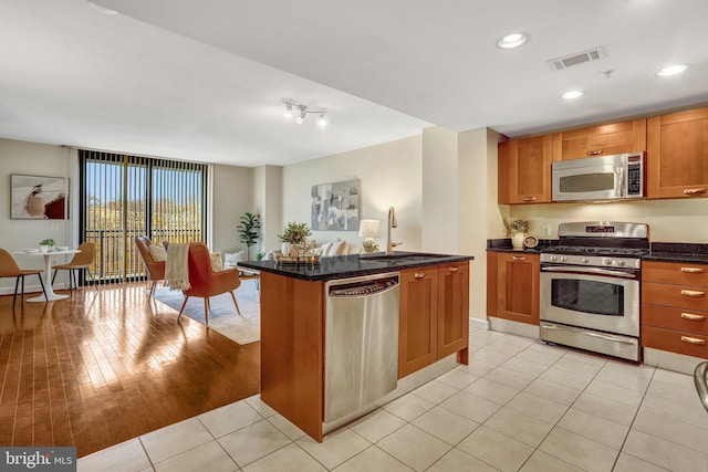 kitchen with sink, a center island with sink, light tile patterned floors, appliances with stainless steel finishes, and dark stone counters