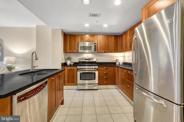 kitchen with appliances with stainless steel finishes, sink, light tile patterned floors, and dark stone counters