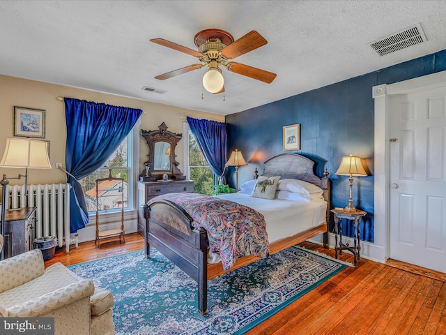 bedroom featuring hardwood / wood-style floors, ceiling fan, radiator heating unit, and a textured ceiling