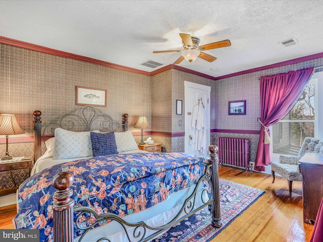 bedroom with hardwood / wood-style floors, radiator heating unit, ceiling fan, crown molding, and a textured ceiling