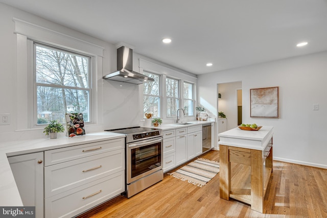 kitchen featuring appliances with stainless steel finishes, white cabinetry, sink, light hardwood / wood-style floors, and wall chimney exhaust hood