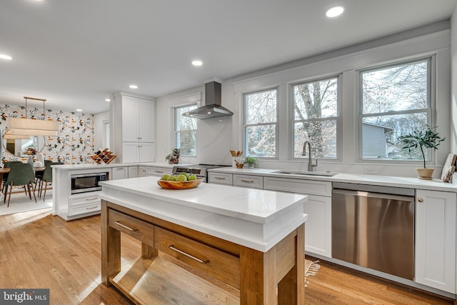 kitchen featuring wall chimney exhaust hood, sink, white cabinetry, light hardwood / wood-style flooring, and stainless steel appliances