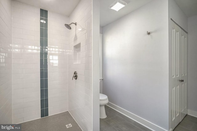 bathroom with tiled shower, toilet, and tile patterned flooring