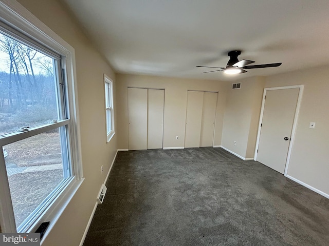 unfurnished bedroom featuring multiple closets, ceiling fan, and dark carpet