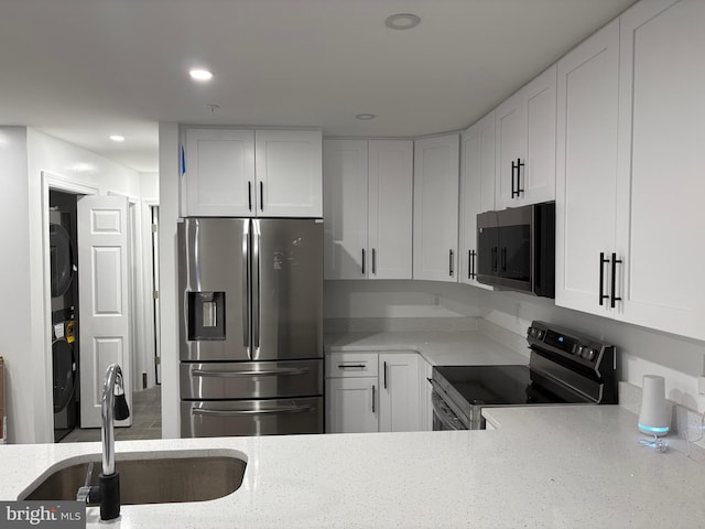 kitchen with stainless steel appliances, stacked washer / dryer, sink, and white cabinets