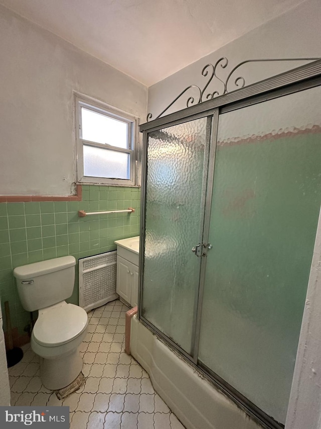 full bathroom featuring radiator, enclosed tub / shower combo, tile walls, vanity, and toilet