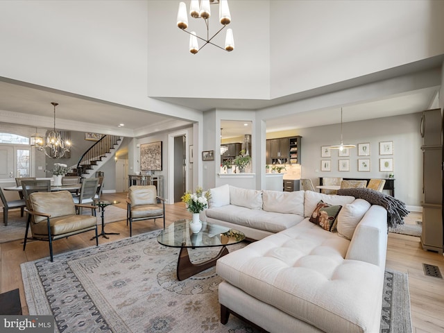 living room featuring visible vents, baseboards, stairs, light wood-style flooring, and an inviting chandelier