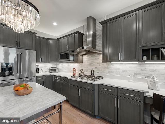 kitchen featuring wall chimney range hood, backsplash, appliances with stainless steel finishes, light wood finished floors, and light countertops