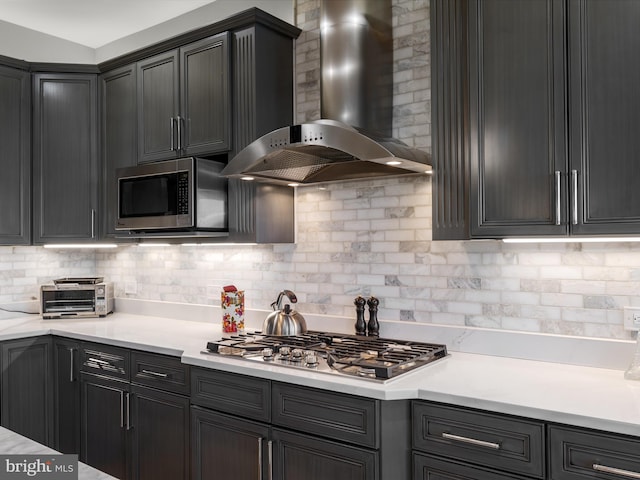 kitchen with a toaster, light countertops, appliances with stainless steel finishes, wall chimney range hood, and tasteful backsplash