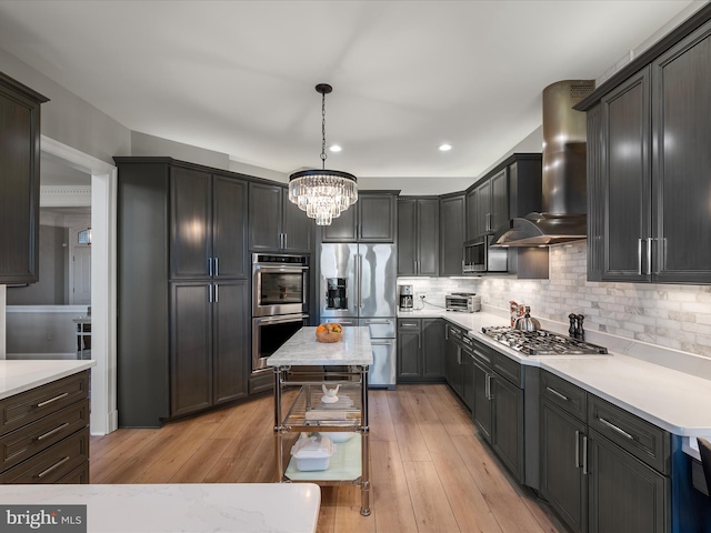 kitchen with backsplash, wall chimney range hood, light wood finished floors, and appliances with stainless steel finishes