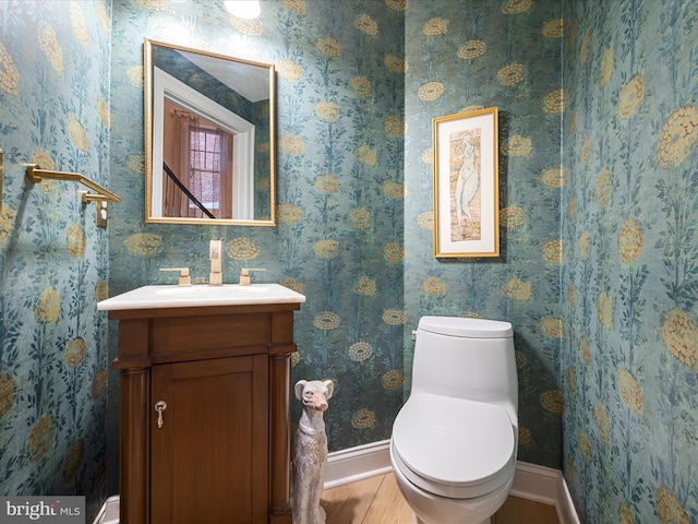 bathroom featuring baseboards, toilet, vanity, and wallpapered walls