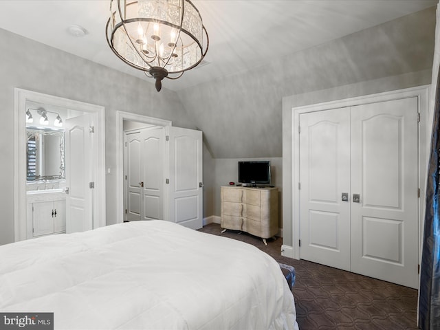 bedroom featuring lofted ceiling, ensuite bath, a closet, an inviting chandelier, and baseboards