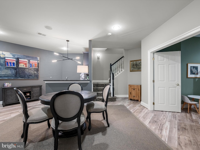 dining space featuring visible vents, a notable chandelier, stairway, light wood finished floors, and baseboards