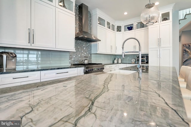 kitchen featuring high end stainless steel range oven, wall chimney exhaust hood, decorative light fixtures, and dark stone counters