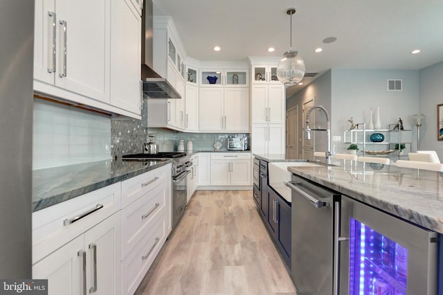 kitchen featuring white cabinetry, dark stone countertops, beverage cooler, stainless steel appliances, and wall chimney exhaust hood