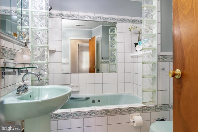 bathroom with tiled tub, sink, tile walls, and toilet