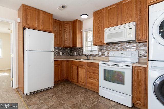 kitchen with tasteful backsplash, white appliances, sink, and stacked washer and dryer