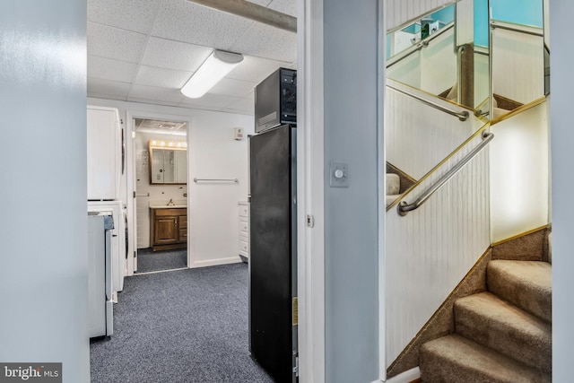 hallway featuring a drop ceiling and dark carpet