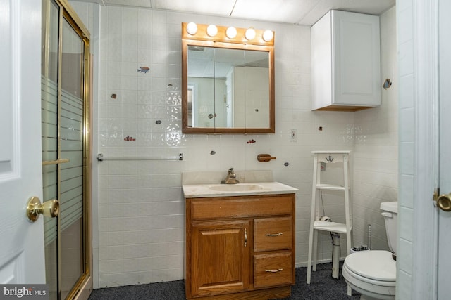 bathroom with a shower with door, vanity, tile walls, and toilet