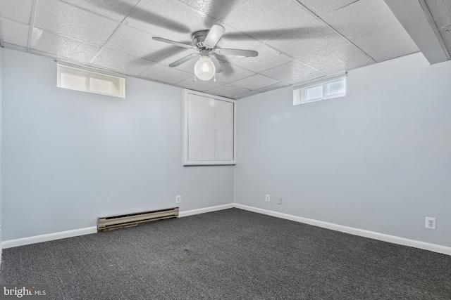 basement featuring dark colored carpet, a baseboard radiator, a drop ceiling, and ceiling fan