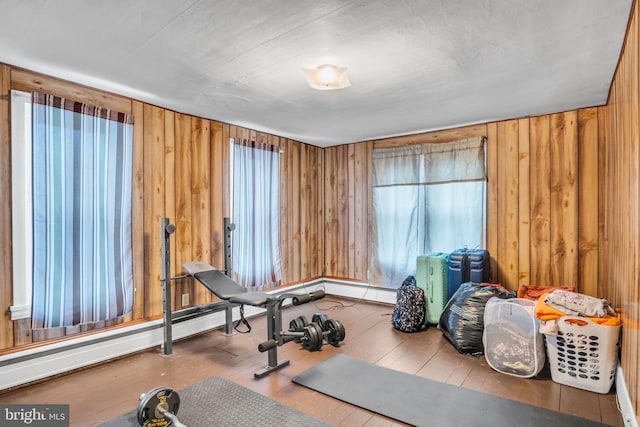 exercise area with a baseboard heating unit, wood-type flooring, and wood walls