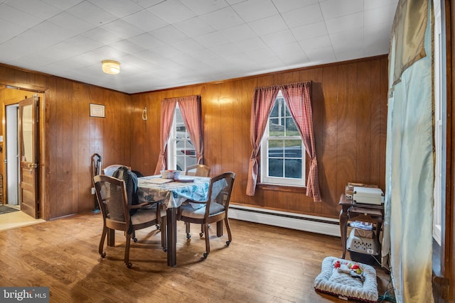 dining area with wood-type flooring, wooden walls, and a baseboard heating unit