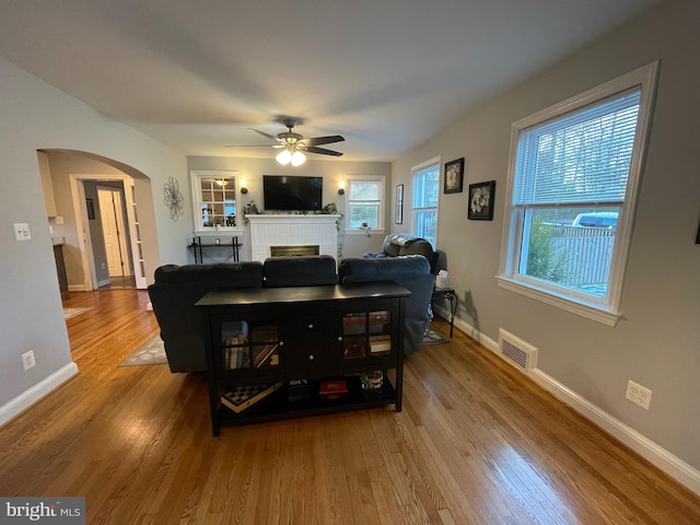 living room featuring a brick fireplace, ceiling fan, and wood-type flooring