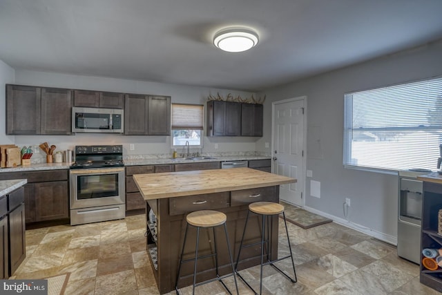 kitchen featuring a kitchen bar, sink, butcher block countertops, dark brown cabinets, and stainless steel appliances