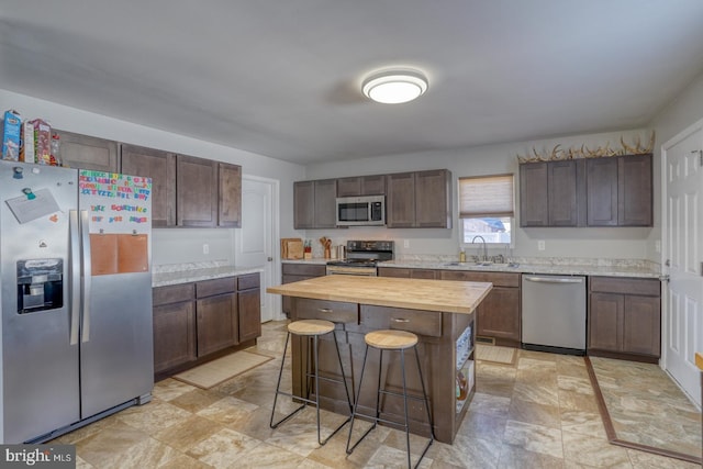 kitchen with a breakfast bar, wood counters, sink, a center island, and stainless steel appliances