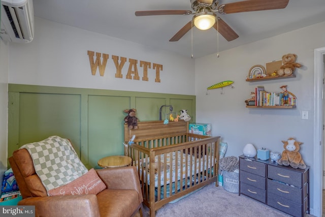 bedroom with a crib, a wall mounted AC, light colored carpet, and ceiling fan