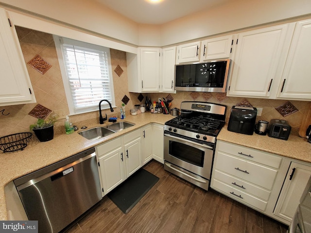 kitchen featuring appliances with stainless steel finishes, tasteful backsplash, dark wood-type flooring, sink, and white cabinetry