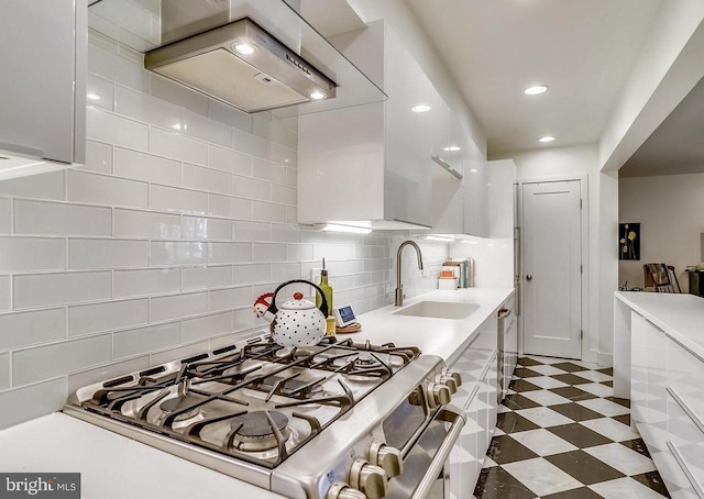 kitchen featuring wall chimney exhaust hood, stainless steel gas range, sink, white cabinetry, and tasteful backsplash